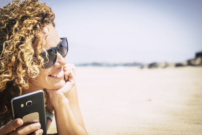 Smiling woman holding mobile phone at beach