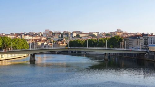 Bridge over river by buildings against clear sky