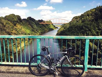 Bicycle on railing by bridge against sky