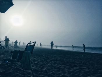 People standing on beach against clear sky during sunset