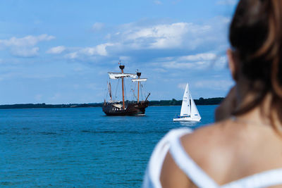 Rear view of woman by sailboats sailing in sea against sky