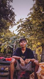 Portrait of young man sitting against trees