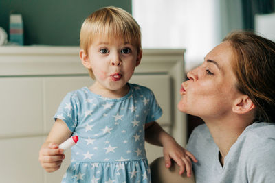 A little girl with painted lips grimaces looking at the camera.