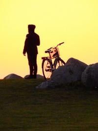 Silhouette man with bicycle standing on landscape against clear sky