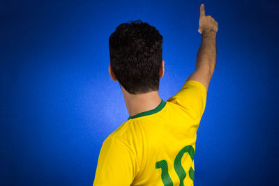 Rear view of man in jersey gesturing while standing against blue background