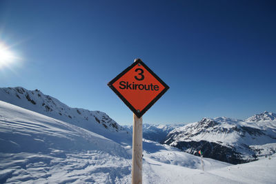 Ski route sign by snowcapped mountains against clear blue sky