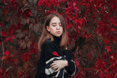 Autumn portrait of a beautiful cute woman against a background of bright red leaves. black sweater