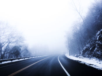 Road amidst trees against sky during winter