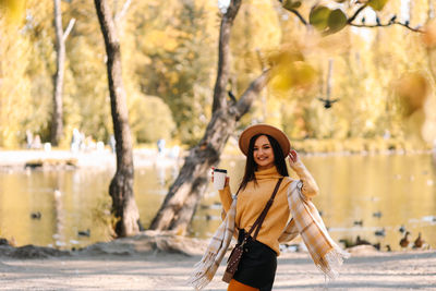 Beautiful smiling girl in casual clothes drinking coffee walking in nature in autumn outdoor