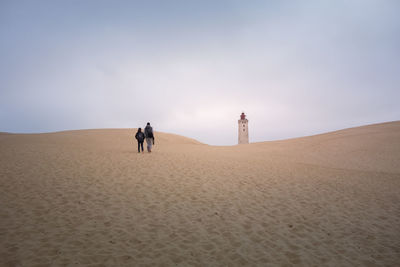 People on sand dune in desert against sky