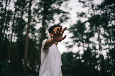 Low angle view of boy showing stop gesture against trees