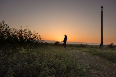 Silhouette person walking on field against sky during sunset