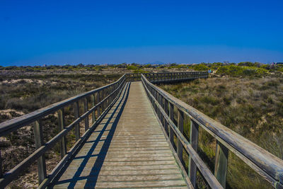 Empty walkway over grassy field against clear sky at lo pagan