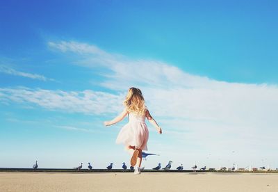 Rear view of girl running at beach by birds against sky