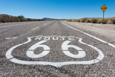 Road 66 sign on road against clear blue sky