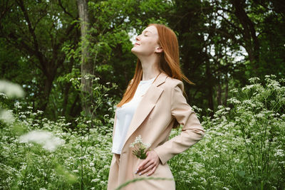 Side view of young woman standing against plants