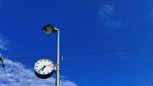 Low angle view of clock on street light against blue sky