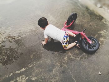High angle view of boy fallen from bicycle on puddle