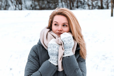 Portrait of young woman sitting on snow covered field