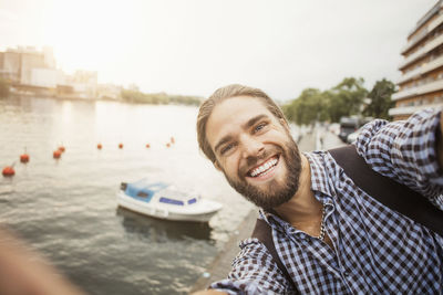 Portrait of smiling man against boat moored at river in city