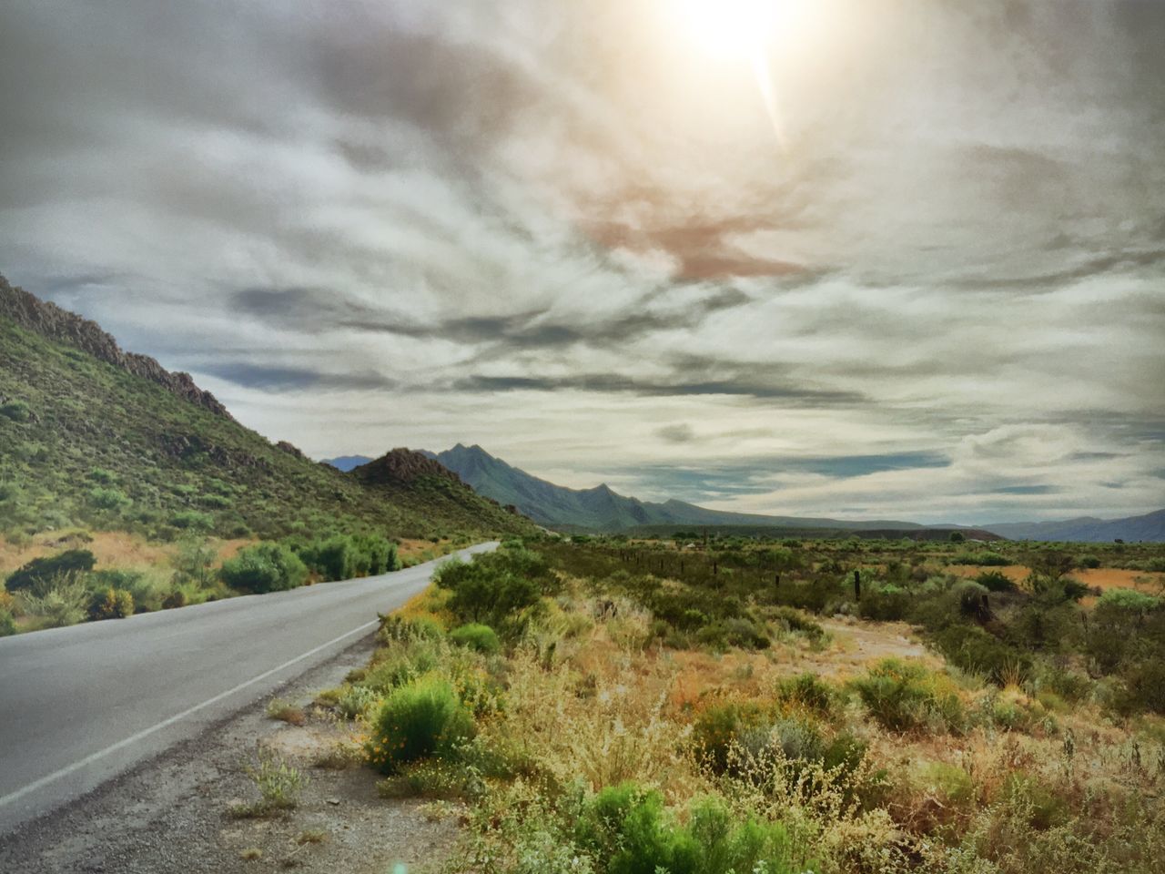 road, the way forward, sky, transportation, mountain, landscape, cloud - sky, tranquil scene, country road, tranquility, scenics, nature, grass, road marking, beauty in nature, cloudy, diminishing perspective, non-urban scene, cloud, empty road