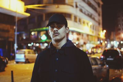 Portrait of young man standing in illuminated city at night