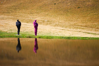 Rear view of people walking on field by lake