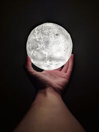 Close-up of hand holding crystal ball against black background