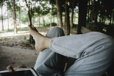 Low section of person using mobile phone while relaxing in forest