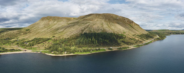 Magnificent scenery of gently sloping mountain on sea coast with road through woodlands at foothill