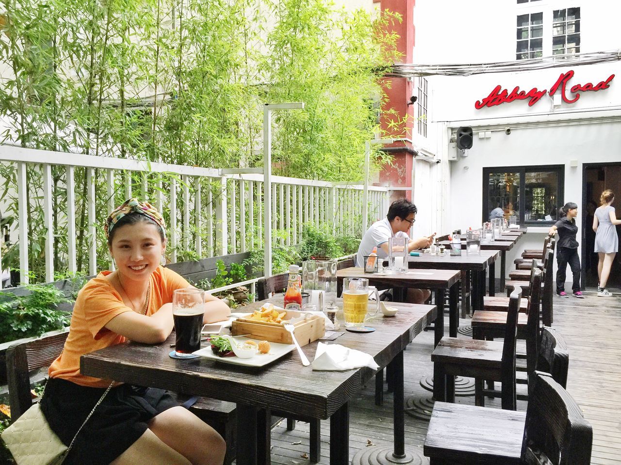 sitting, lifestyles, leisure activity, table, built structure, architecture, building exterior, chair, relaxation, casual clothing, tree, day, person, sunlight, young adult, incidental people, outdoors, food and drink