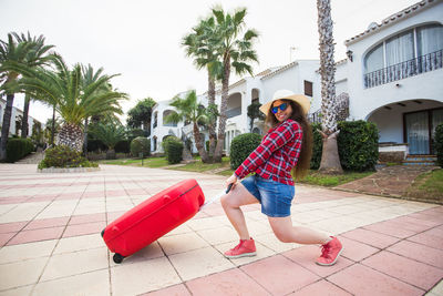 Full length of young woman standing by palm trees