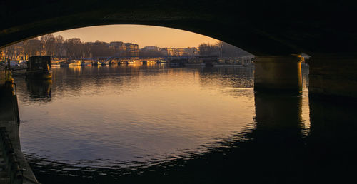 Arch bridge over river in city against sky at sunset