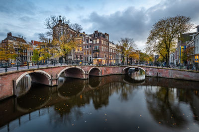 Bridge over river by buildings against sky