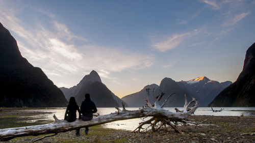 Rear view of couple sitting by lake against sky