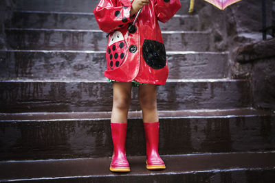 Low section of girl wearing red raincoat and boots while standing on steps