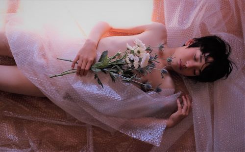 High angle view of naked boy holding flowers while lying with bubble wrap on floor