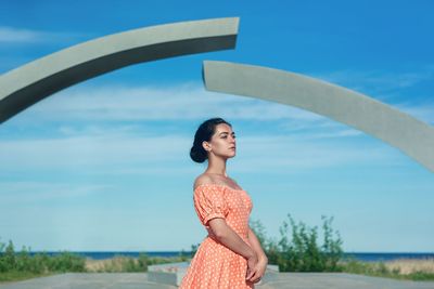 Mid adult woman looking away while standing against blue sky