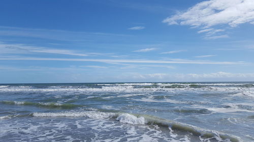 Waves splashing in sea against cloudy sky