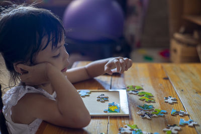 Cute girl playing with puzzle on table