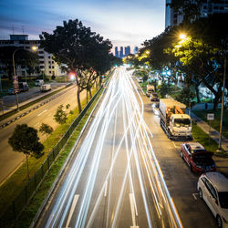 Light trails on road by street in city against sky