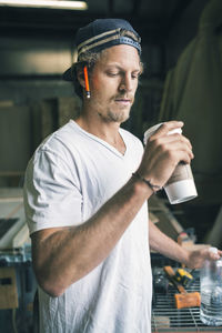 Carpenter holding disposable coffee cup and water bottle in workshop