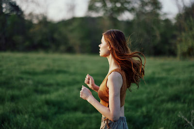 Young woman looking away while standing on field