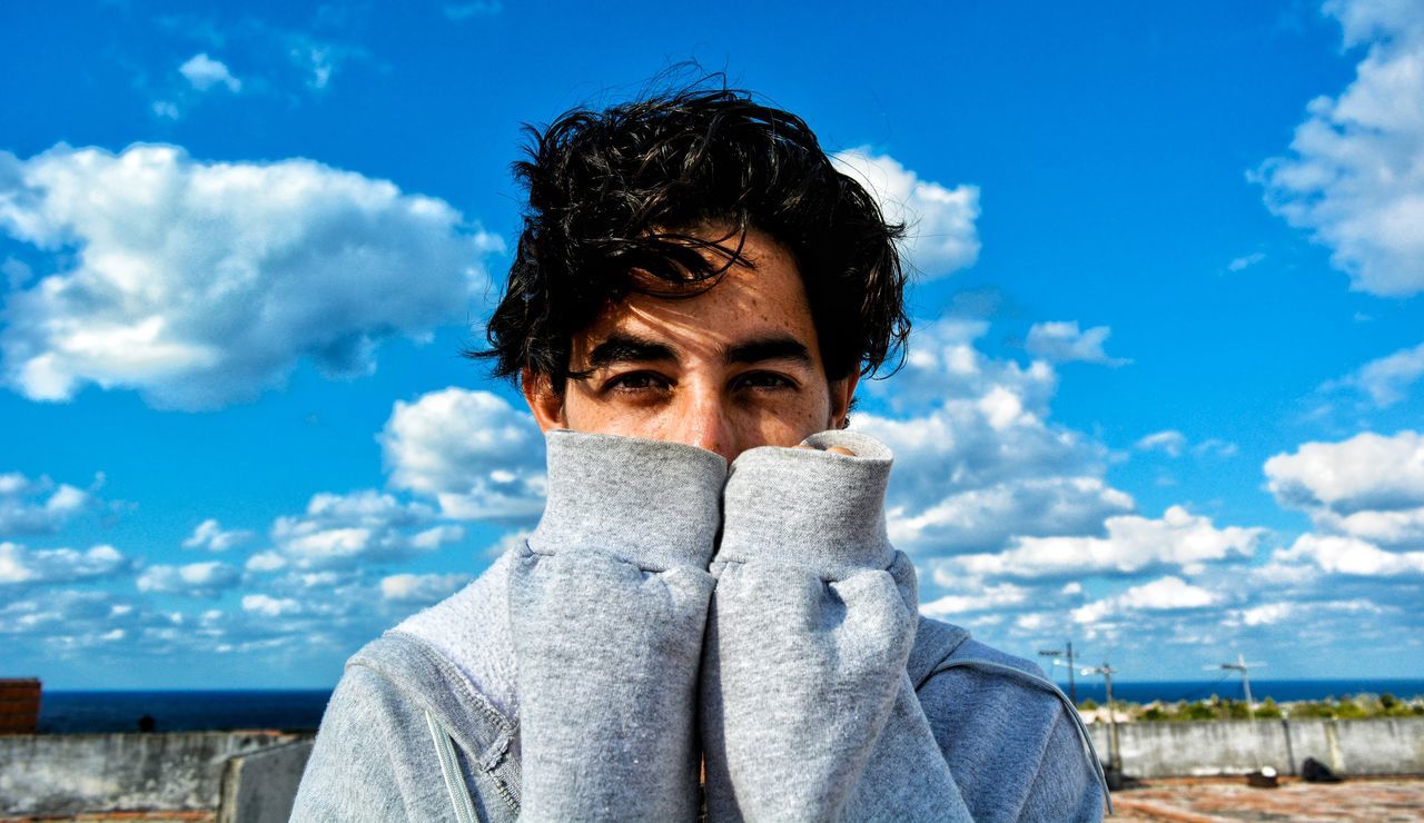 sky, cloud - sky, portrait, one person, looking at camera, headshot, real people, young adult, front view, lifestyles, nature, day, leisure activity, covering, obscured face, focus on foreground, blue, black hair, scarf, warm clothing