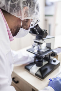 Close-up side view of man scientist looking through microscope at laboratory