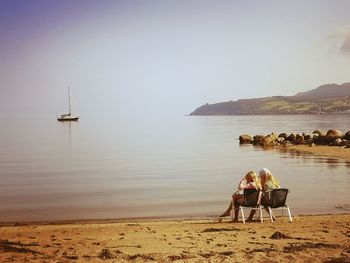 Rear view of woman sitting on beach against sky