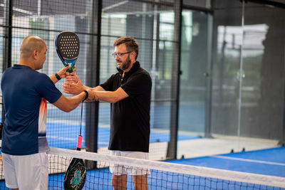 Monitor teaching padel class to man, his student - trainer teaches boy how to play padel on indoor 