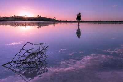 Silhouette woman by lake against sky during sunset