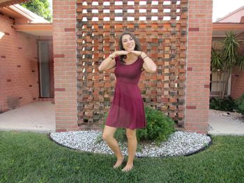 Full length portrait of a smiling young woman standing against brick wall