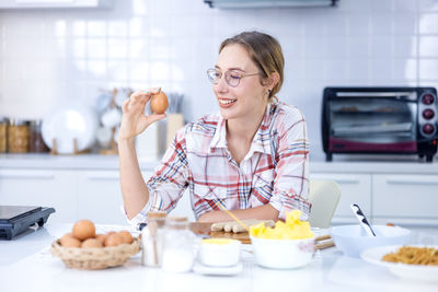 Shot of beautiful young woman showing brown chicken egg with hands in at kitchen home.